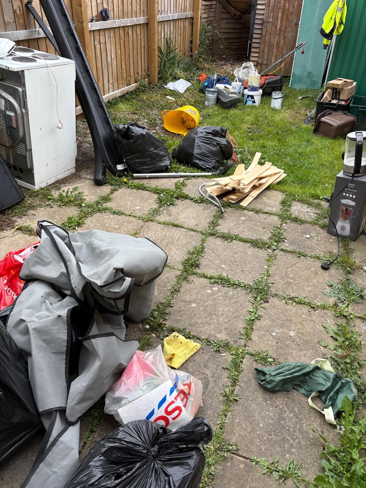 A cluttered rear yard part-way through clearance, with bagged waste and separated items